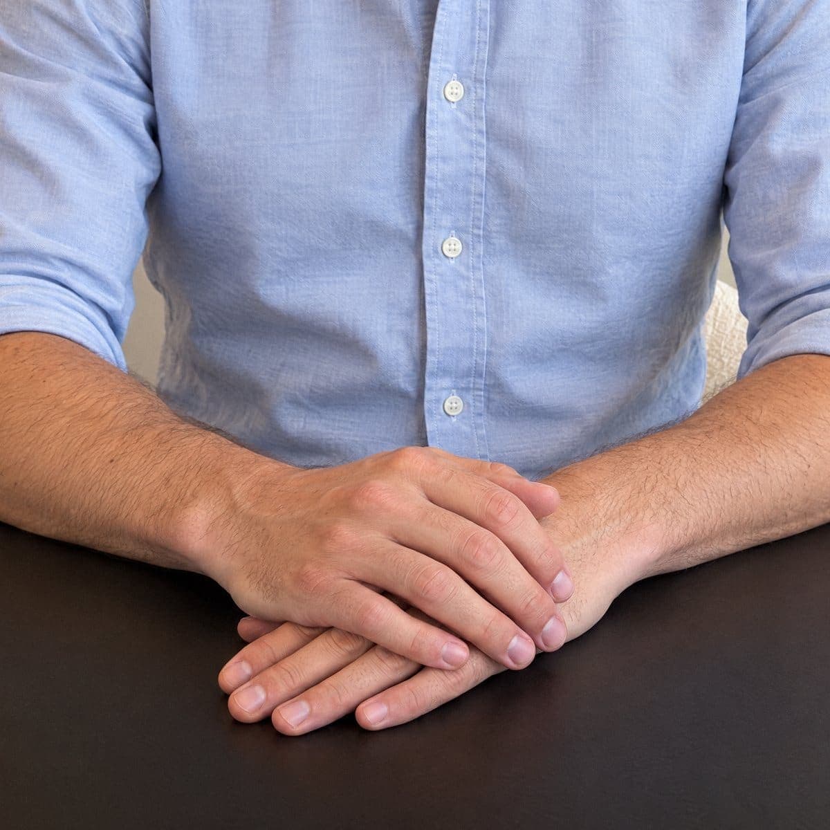 Mãos do Dr. Vogel pousadas calmamente uma sobre a outra na mesa preta do estúdio